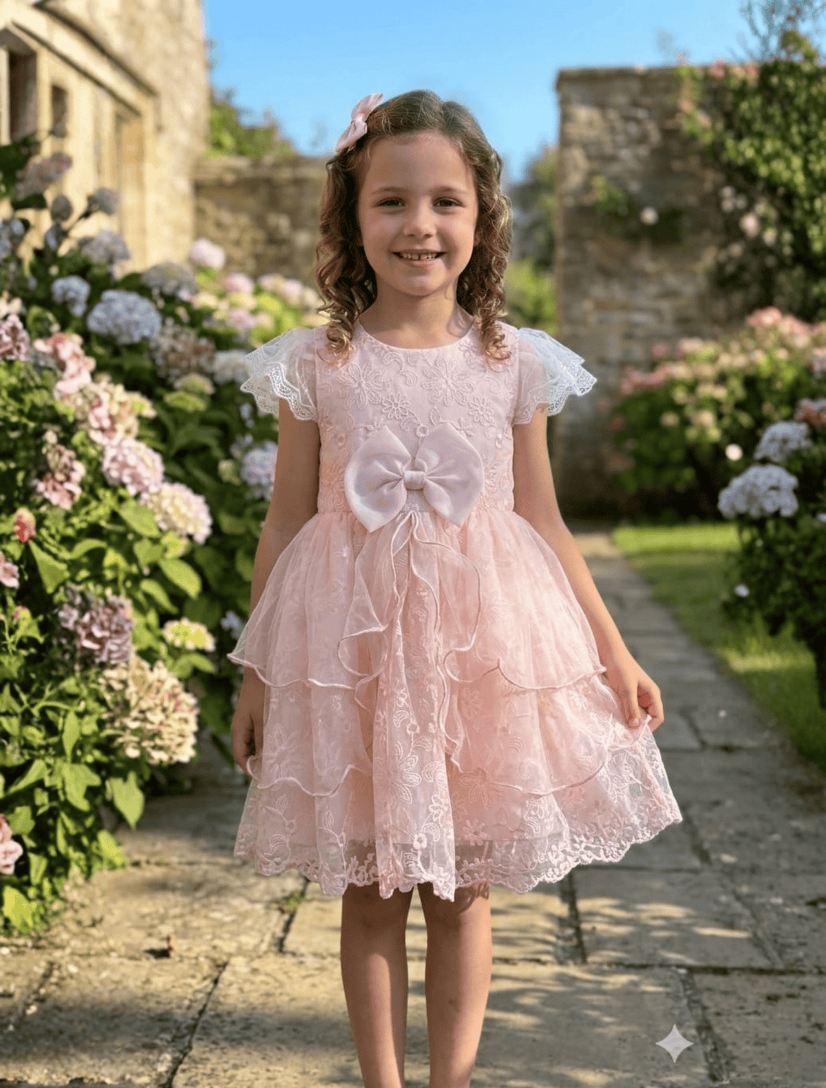 whisperingpoppers summer frocks Blush Pink Lace Net Party Frock with Tiered Tulle Skirt & Bow — Girls 3 to 8 Years.girl is showing front side of the dress.embrodered soft net with silk bow on front waist .soft breathable impoted fabric dress.wear in weddings, event, birthdays,parties and functions. soft inneer linning to wear in pakistani summer season.perfect for all seasons